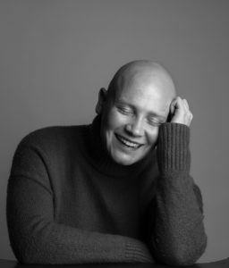 Black and white photo of Joyce looking down and laughing, her head rests on one hand